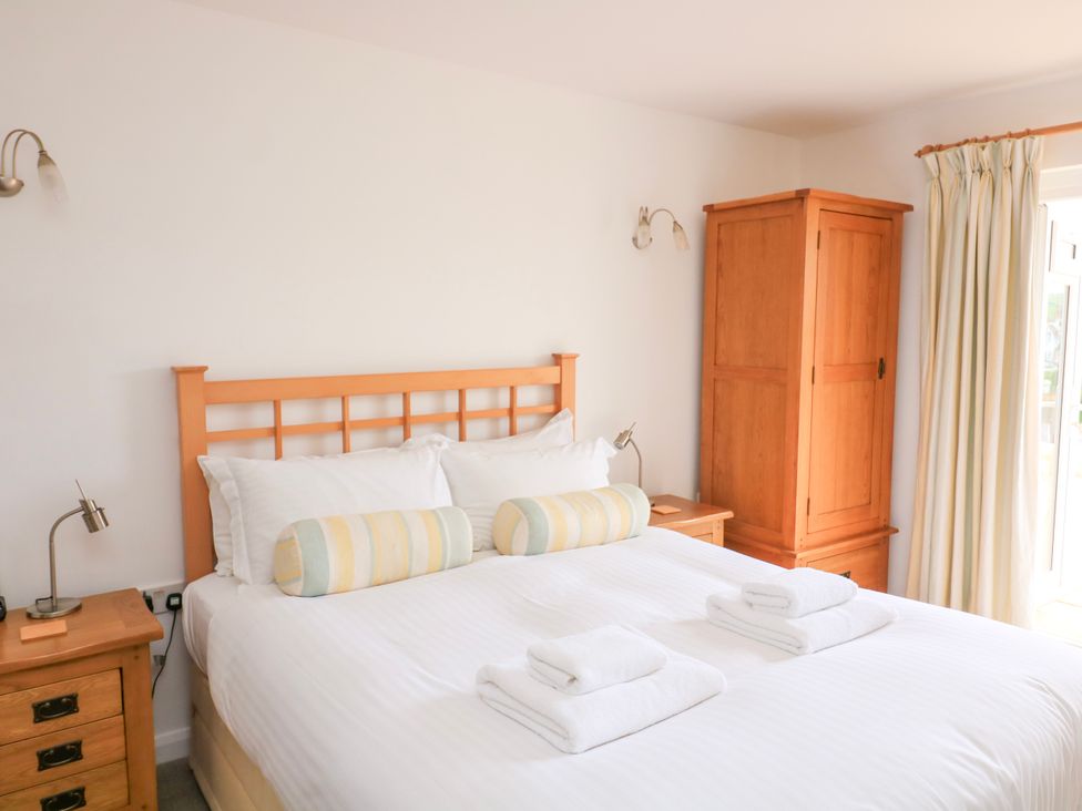 A bedroom with a double bed white bedding two striped bolster pillows wooden bedside tables and a wooden wardrobe at 2 Sea Gardens in Hope Cove