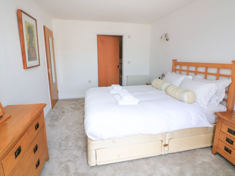 A bedroom with a bed with white linens and pillows a wooden dresser and nightstand and a framed picture on the wall at 2 Sea Gardens in Hope Cove