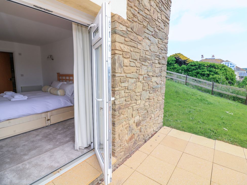A bedroom with a bed and folded towels visible through an open glass door leading to a tiled patio and grassy area at 2 Sea Gardens in Hope Cove