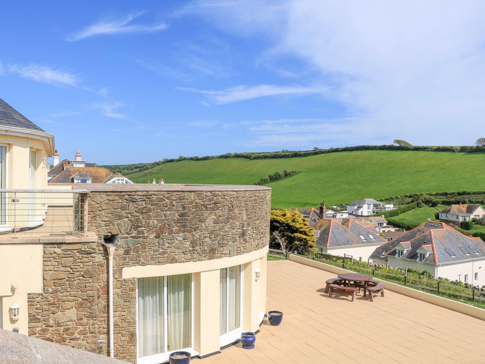 A terrace with a round wooden picnic table and stone wall overlooking green hills and houses at 2 Sea Gardens in Hope Cove