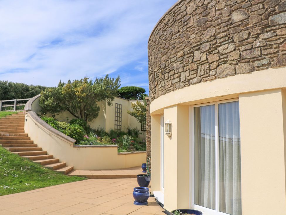 An exterior view of a stone and cream building with sliding glass doors a staircase and garden area at 2 Sea Gardens in Hope Cove