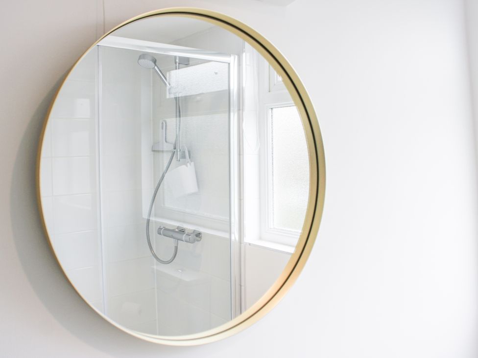 A bathroom with a shower and a round mirror at 4 Lyndhurst Salcombe