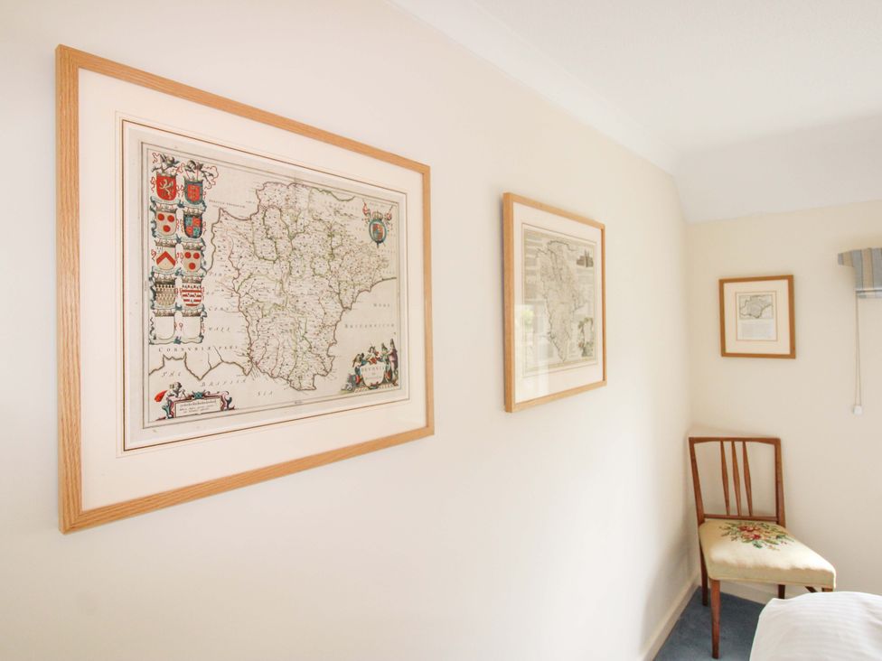 A bedroom with framed maps and a wooden chair at Orchard Barn Salcombe