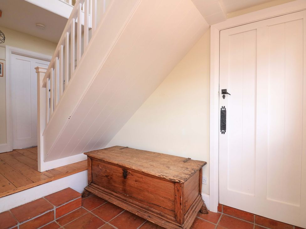 A hallway with a staircase, wooden chest, and door at Savernake in Thurlestone