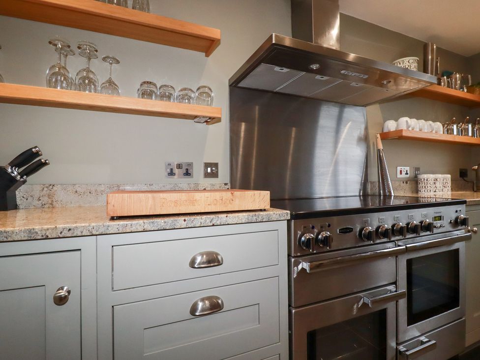 A kitchen with cabinets, stove, and glasses on shelves at Postcard Lodge in Polruan