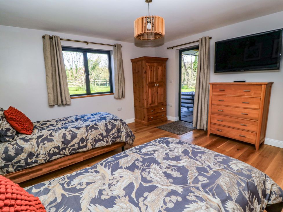 A bedroom with two beds, a wardrobe, and a television at The Old Dairy Cotleigh near Honiton