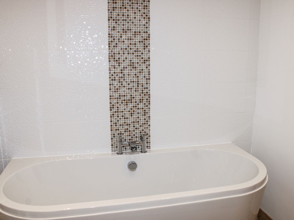 A bathtub with a mosaic wall in a bathroom at 4 Ocean Reach in Bolberry