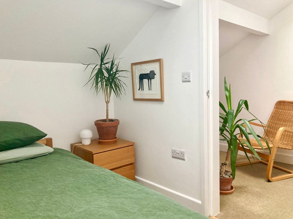 A bedroom with a bed, bedside table, plant, and chair at The Old Riverside School House Apt 5 Hebden Bridge