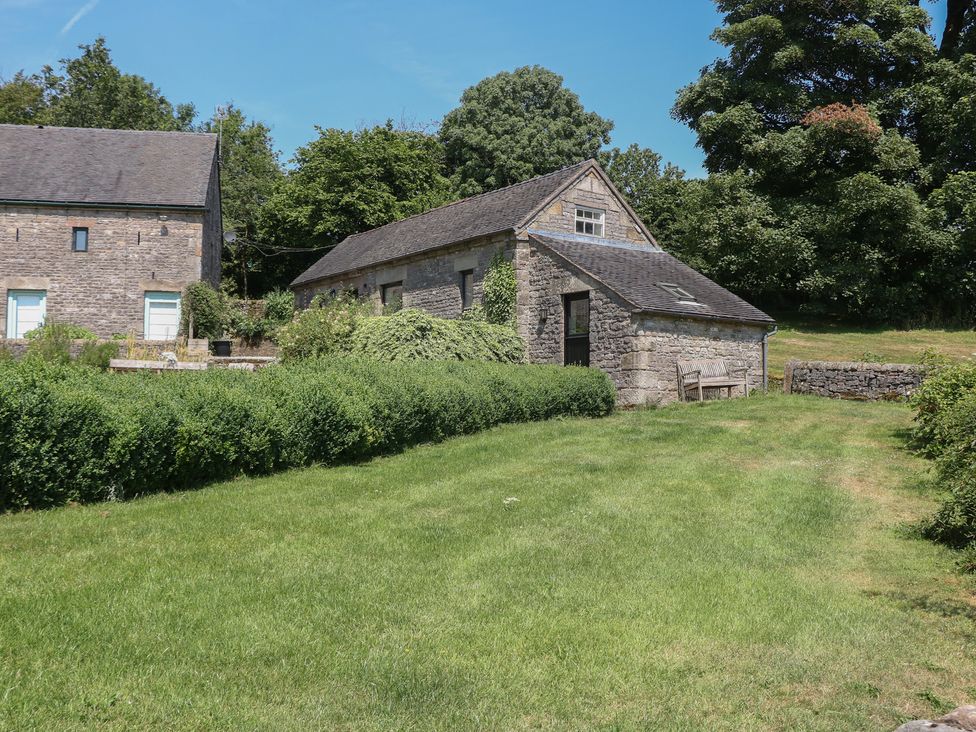 A stone building and bench in a garden at Slade Tops in Ilam