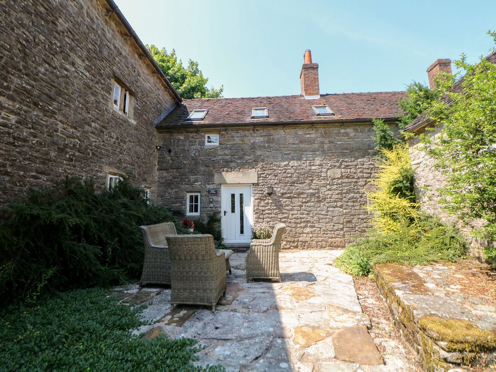 An outdoor area with stone wall and chairs at Slade Cottage in Ilam