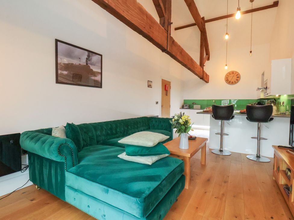 A living room with a green sofa and a kitchen area at Repton @ Engine Shed in Whitby