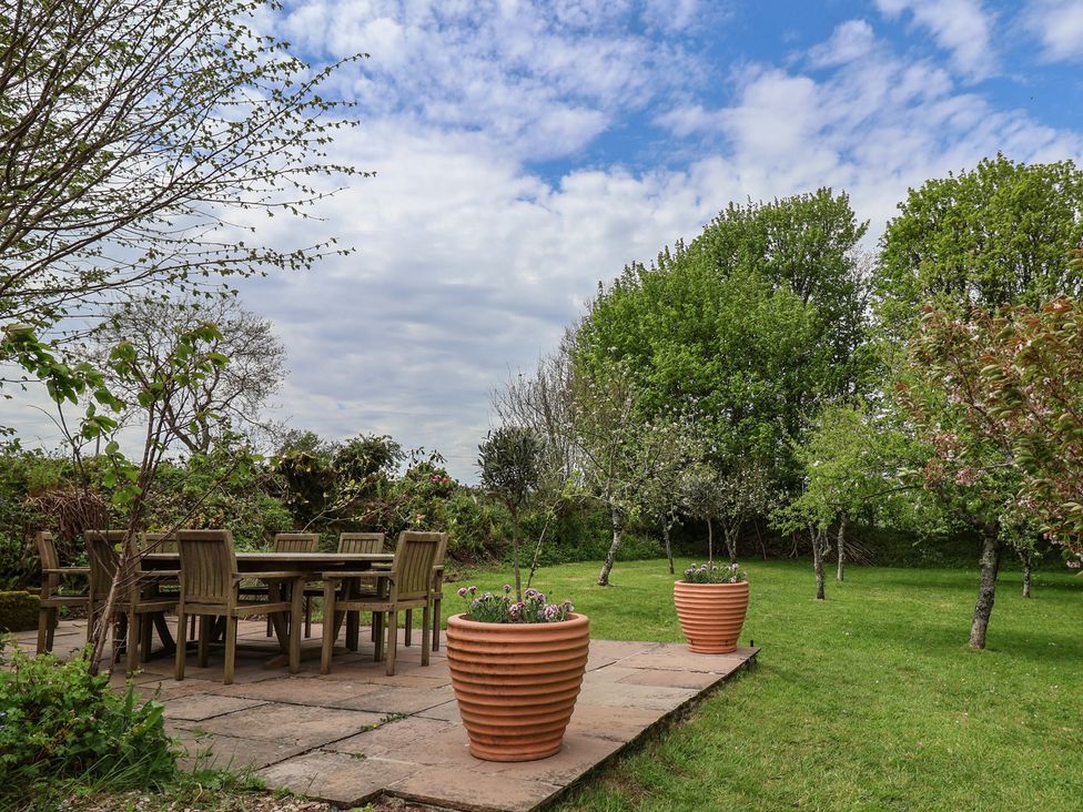 A garden with a table and chairs surrounded by trees and flower pots at Hook Cottage in Pelynt near Looe