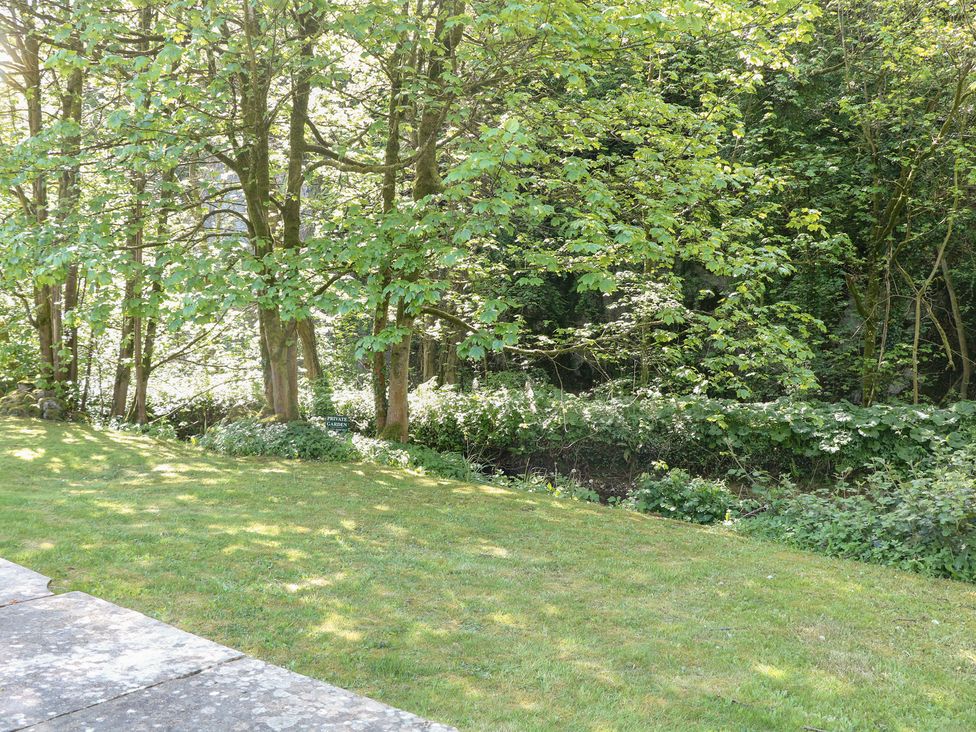 A garden with grass and trees adjacent to a stream at Wye Apartment, Litton Mill in Miller's Dale