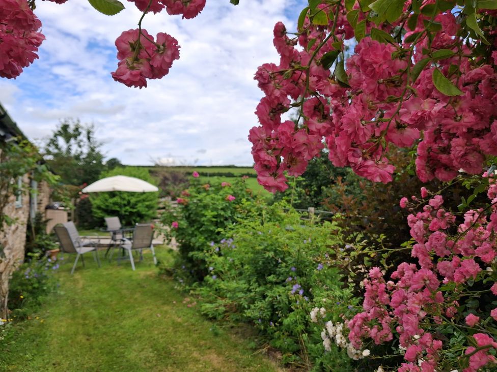 A garden with a table and chairs under an umbrella at Owl Barn Tavistock