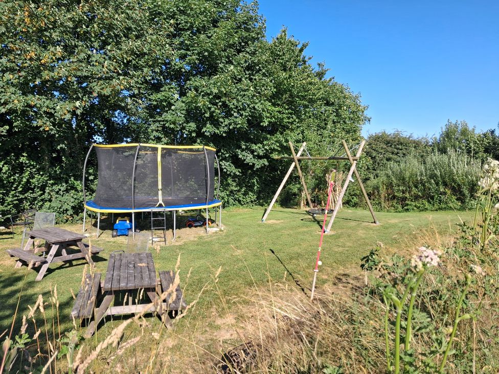 An outdoor playground with a trampoline and swing set at Owl Barn in Tavistock